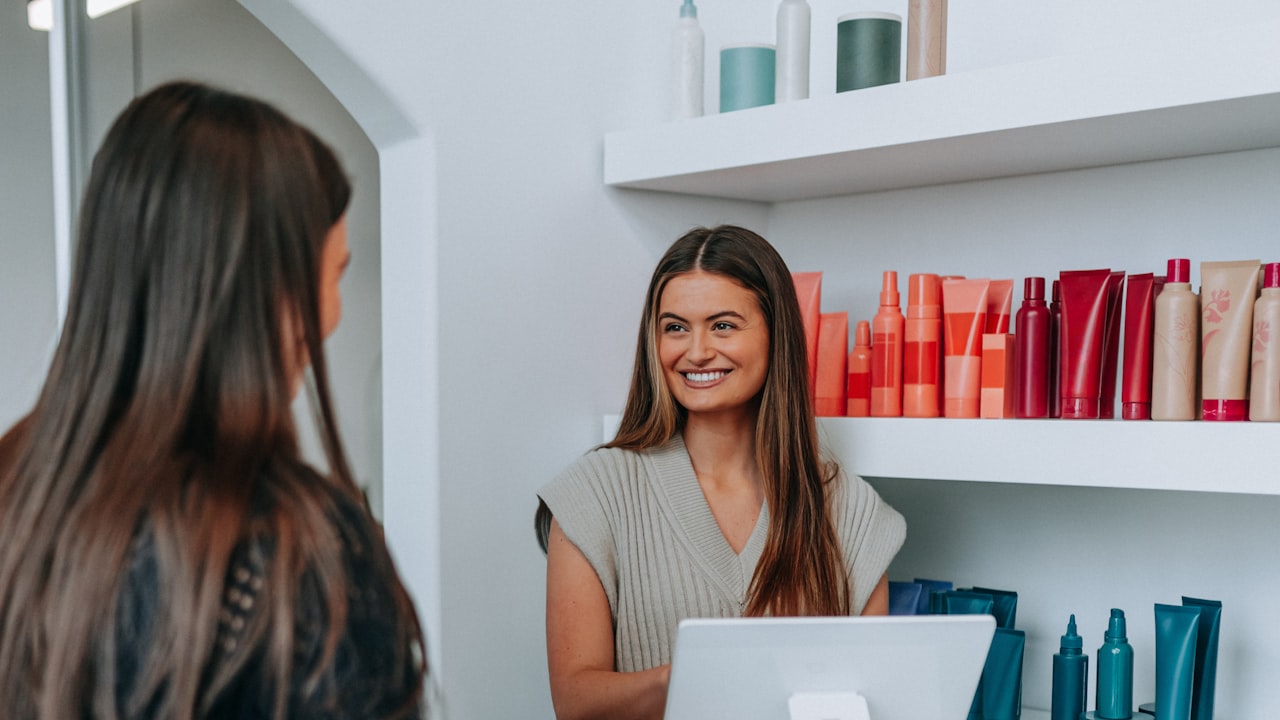 A salon owner smiling at a customer across the front counter beside the card reader