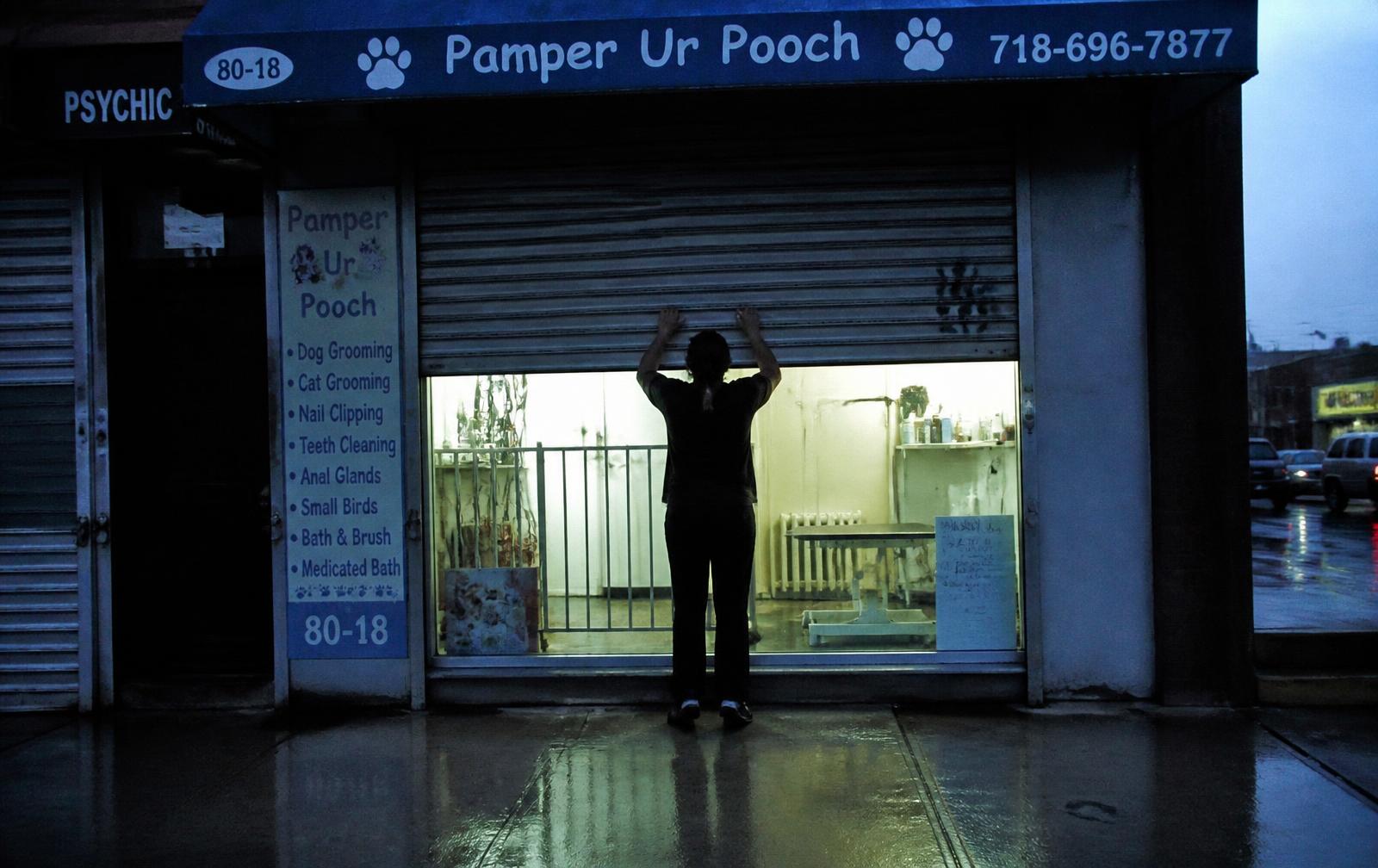 A groomer pulling up the shutter of a small storefront before opening, early morning