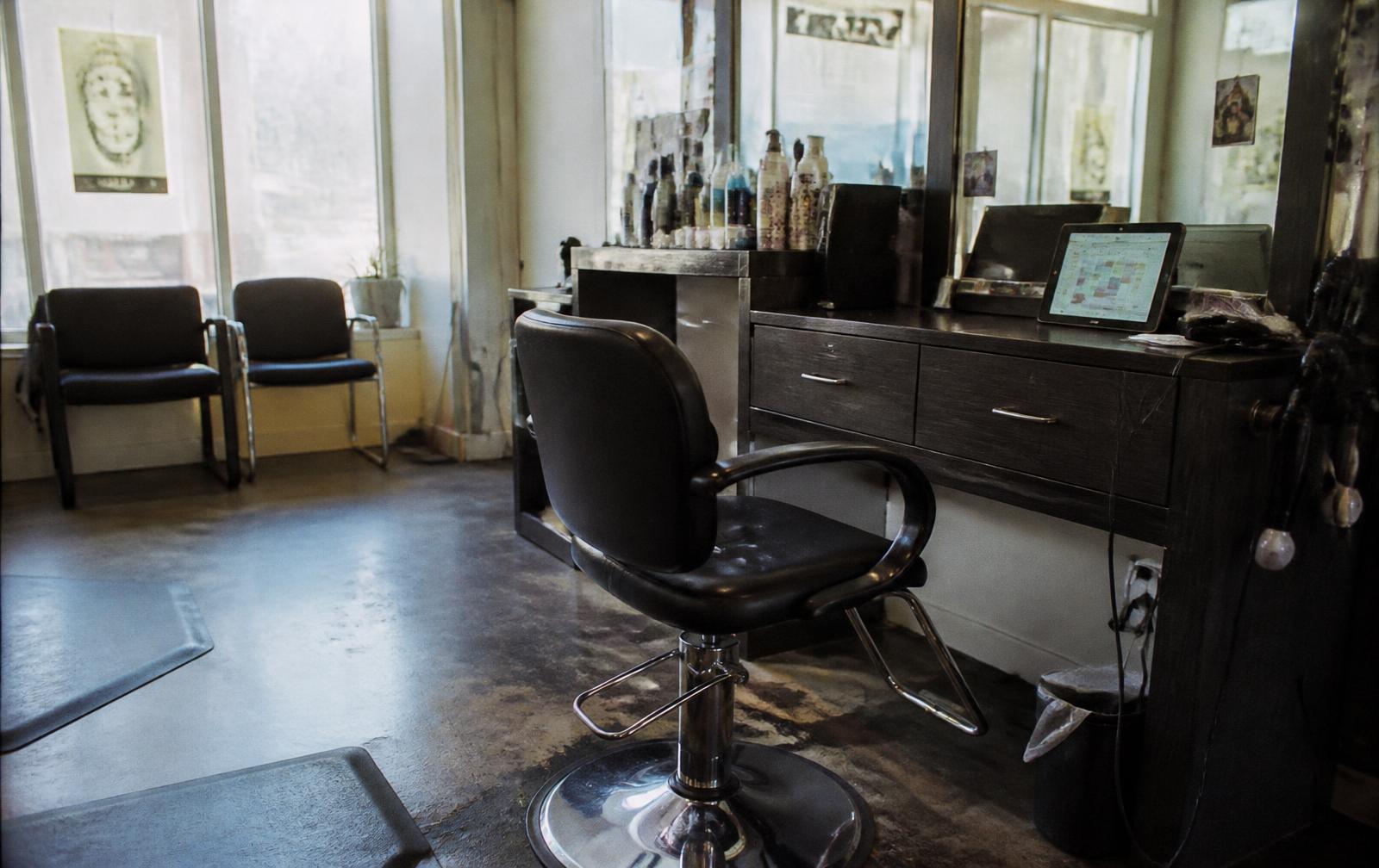 An empty styling chair in a quiet salon with a booking calendar open on a tablet