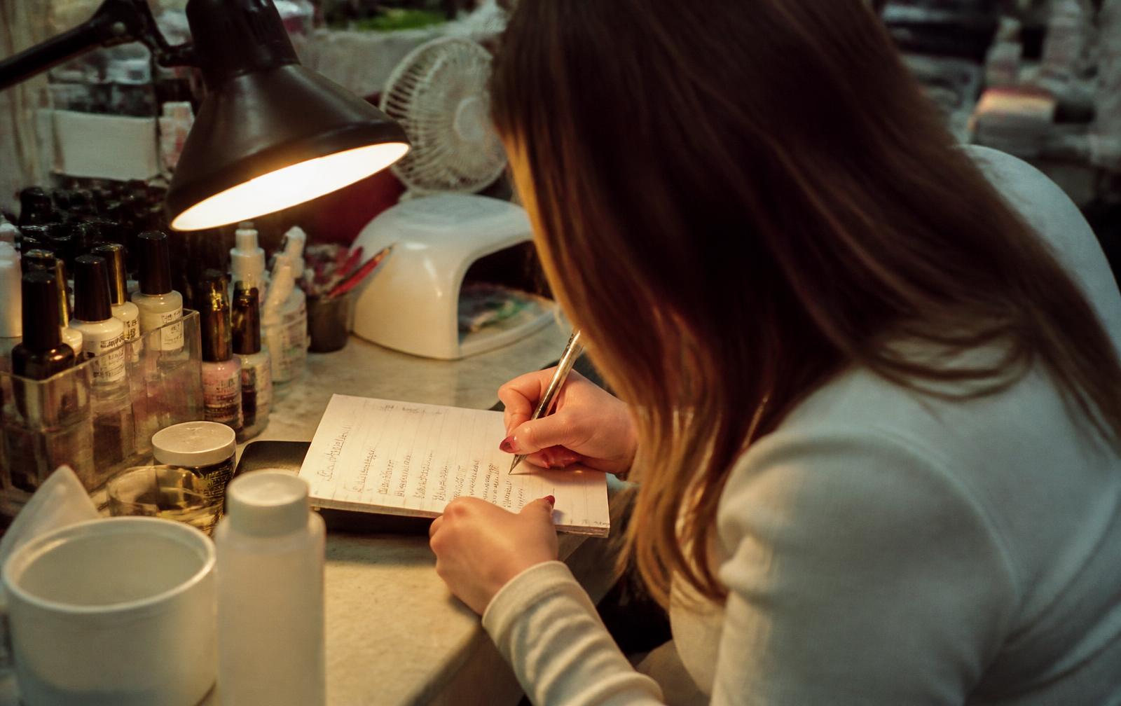 A nail technician writing a service price list in a notebook at her station