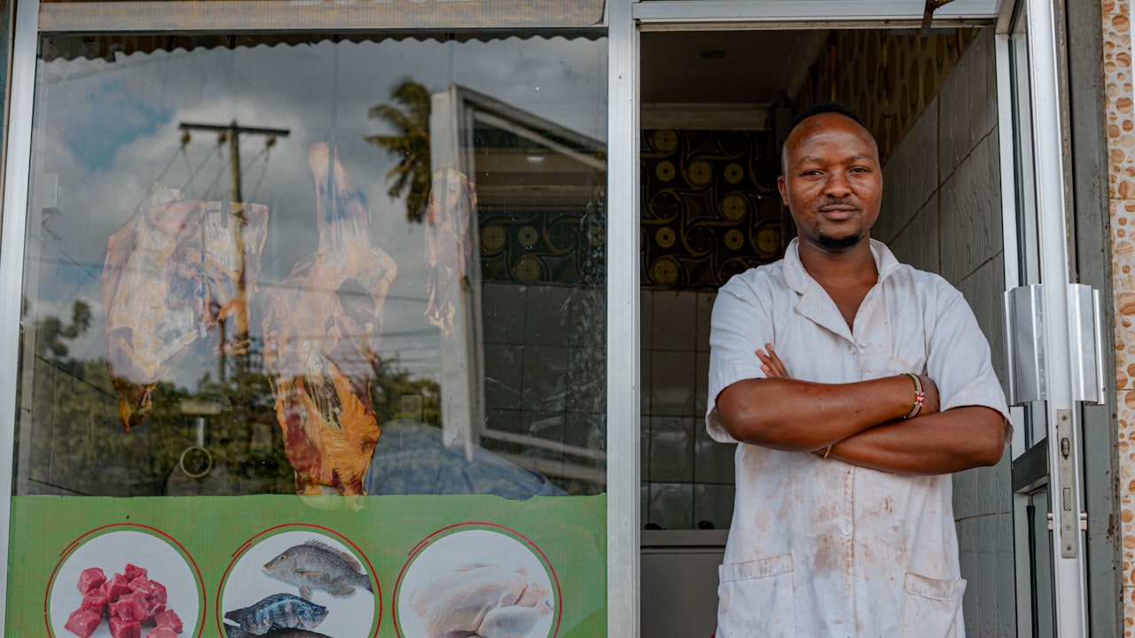 A confident local shop owner standing in the doorway of their store