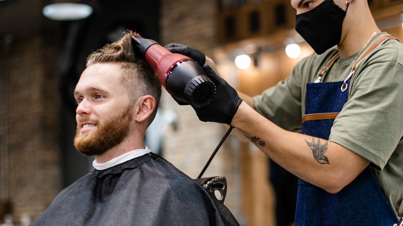 A barber blow-drying a client's fresh haircut in a modern barbershop