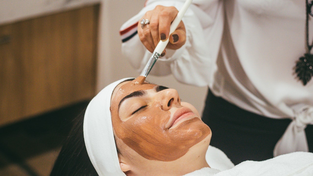 An esthetician brushing a facial mask onto a relaxed client's face
