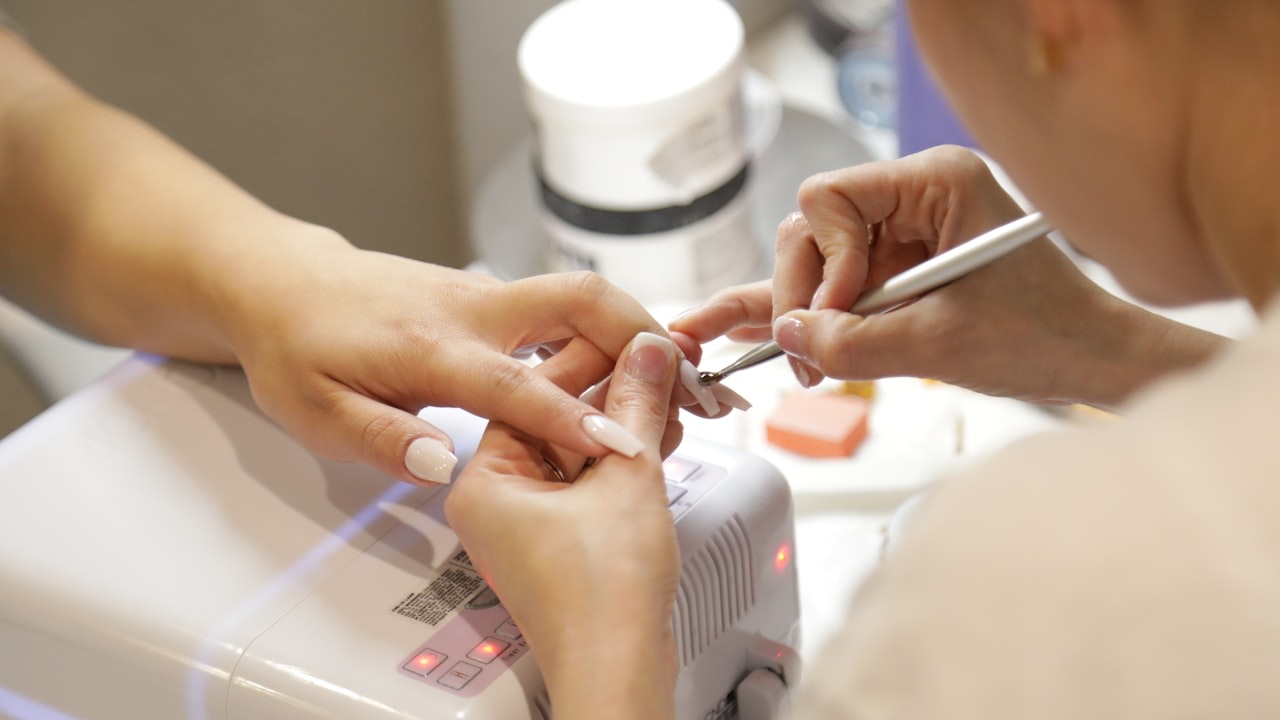 A nail technician shaping a client's nails at a manicure station