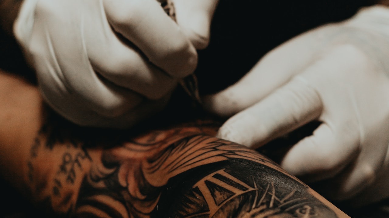 A gloved tattoo artist working on a detailed arm sleeve